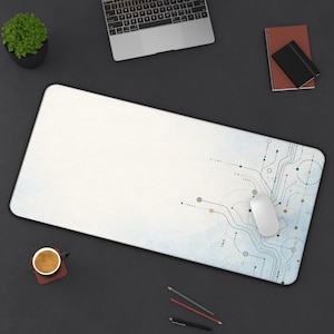 May include: A rectangular desk mat featuring a white and light blue watercolor background with a dark blue circuit board pattern on the right side. A white computer mouse rests on the mat, which is positioned on a dark gray surface.