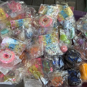 K&ouml;nnte beinhalten: Eine Sammlung verschiedener sensorischer Fidget-Spielzeuge, darunter weiche Donuts, Netzb&auml;lle und verschiedene strukturierte Formen, einzeln verpackt in durchsichtigen Plastikt&uuml;ten mit bunten Markenetiketten, die Symbole und den Text Puni zeigen.