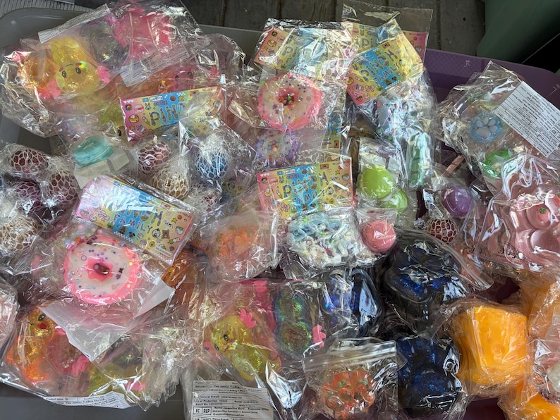 K&ouml;nnte beinhalten: Eine Sammlung verschiedener sensorischer Fidget-Spielzeuge, darunter weiche Donuts, Netzb&auml;lle und verschiedene strukturierte Formen, einzeln verpackt in durchsichtigen Plastikt&uuml;ten mit bunten Markenetiketten, die Symbole und den Text Puni zeigen.
