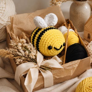 Peut inclure: Une abeille au crochet jaune et noir avec des ailes blanches dans une bo&icirc;te cadeau. La bo&icirc;te contient de la laine, un crochet et des fleurs s&eacute;ch&eacute;es. L'abeille a un visage souriant. La bo&icirc;te est attach&eacute;e avec un ruban cr&egrave;me.