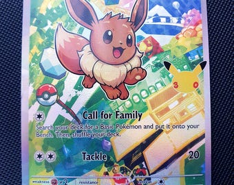 Puede incluir: Una carta coleccionable holográfica de Eevee que muestra al personaje en el centro con 60 HP. La carta presenta el texto Call for Family y Tackle, junto con un logotipo del 25 aniversario. El fondo es un diseño geométrico abstracto y colorido.