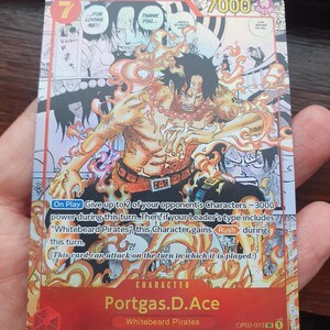 May include: A trading card featuring the character Portgas D. Ace from the "Whitebeard Pirates" series. The card has a red and orange color scheme with the number 7 in the top left corner and the text "7000" in the top right. The card includes text and illustrations.