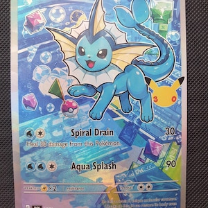 Könnte beinhalten: Eine Vaporeon-Sammelkarte mit einem blauen Wasserwesen mit weißem Kragen und flossenartigen Ohren. Die Karte zeigt 120 KP, die Attacken Spiral Drain und Aqua Splash sowie ein kleines gelbes Pikachu-Symbol auf der rechten Seite.