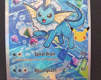 Puede incluir: Una carta coleccionable de Vaporeon que muestra una criatura acuática azul con un cuello blanco y orejas en forma de aleta. La carta muestra 120 HP, los ataques Spiral Drain y Aqua Splash, y un icono de silueta de Pikachu amarillo a la derecha.