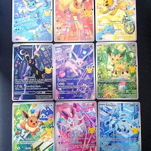 Puede incluir: Una colección de nueve cartas coleccionables rectangulares con coloridas ilustraciones de varias criaturas. Cada carta muestra un personaje único, nombres de ataques, valores de daño y un pequeño logo dorado de aniversario.