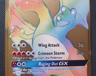 Puede incluir: Una carta coleccionable Charizard GX de color dorado con una ilustración de dragón en tonos arcoíris. La carta muestra 250 HP, ataques llamados Wing Attack, Crimson Storm y Raging Out GX, junto con varias estadísticas de juego y texto impreso.