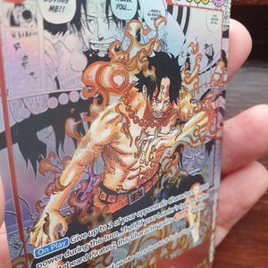 May include: A trading card featuring the character Portgas D. Ace from the "One Piece" series. The card has a vibrant design with Ace surrounded by flames. The card's text includes "7000" and "Whitebeard Pirates."
