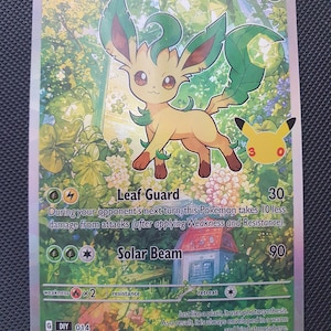 May include: A Leafeon trading card featuring a tan and green creature standing in a lush garden with a small house. The card displays 110 HP, the attacks Leaf Guard and Solar Beam, and a 25th-anniversary Pikachu logo with the number 30 in the corner.