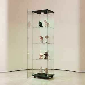Puede incluir: Una vitrina alta de vidrio transparente con tapa y base negras, que exhibe varias figuras en estantes de vidrio. El gabinete está sobre ruedas y tiene un diseño moderno, perfecto para exhibir objetos de colección. Las figuras incluyen un dinosaurio verde, un conejo y figuras de astronautas.