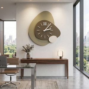 Puede incluir: Un reloj de pared moderno con un diseño único. El reloj presenta una esfera marrón con manecillas y marcadores blancos, sobre un fondo de formas superpuestas en verde oliva y blanco roto. El reloj está montado en una pared blanca.
