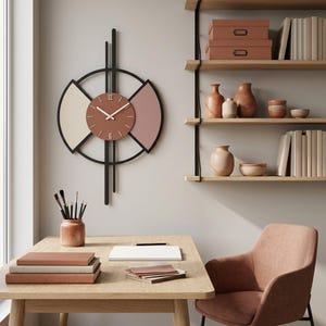May include: A contemporary wall clock with a circular design, featuring a brown clock face and a black frame. The clock has a cream and pink accent. The clock is hanging on a light grey wall. The clock is approximately 30 cm in diameter.