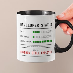 Peut inclure: Mug en céramique blanche avec intérieur et anse noirs. Le mug affiche le texte "DEVELOPER STATUS" et un graphique montrant les niveaux de compétence, de confiance et de syndrome de l'imposteur. L'état est "SOMEHOW STILL EMPLOYED."