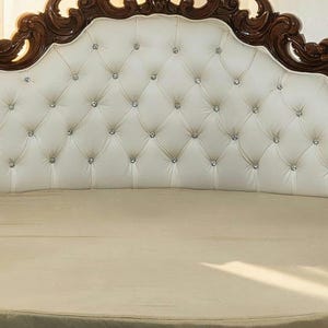 Close-up of an ornate hand-carved solid teak wood headboard with deep white button-tufted upholstery and crystal accents.