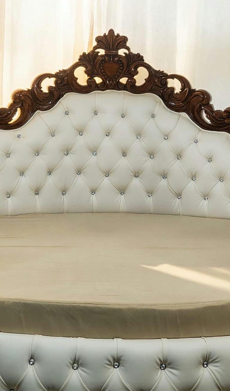 Close-up of an ornate hand-carved solid teak wood headboard with deep white button-tufted upholstery and crystal accents.