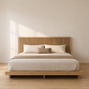 May include: A low-profile wooden platform bed frame featuring a vertical slat headboard. The bed is dressed in light beige bedding, including two large rectangular pillows and a smaller, centered brown accent pillow with a matching brown runner.