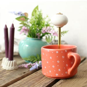 Può includere: Una tazza di ceramica bianca con manico nero e la scritta "But First, Coffee" in stile scritto a mano. La tazza è su una superficie bianca. La tazza è alta circa 10 cm.