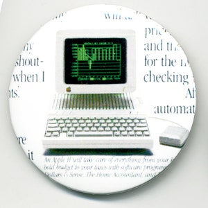 May include: A white, circular button featuring a vintage Apple II computer with a green screen displaying a graph. The button has text from a newspaper article surrounding the computer. A mouse is visible.