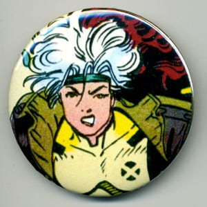 Può includere: Bottone rotondo con un'illustrazione di fumetti di un personaggio con capelli bianchi, una fascia verde e un abito giallo e verde. Il personaggio ha un'espressione arrabbiata. Lo sfondo ha elementi rossi e neri.