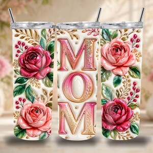 May include: A set of three stainless steel tumblers with lids and straws. Each tumbler features a floral design with roses and the word "MOM" in a decorative font. The tumblers are white with gold and pink accents.