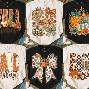 May include: A collection of six short-sleeve t-shirts in black and cream, featuring various graphic prints including pumpkins, bows, flowers, cowboy boots, and the text FALL VIBES, displayed in a grid layout on a textured surface.