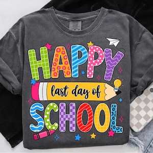 以下が含まれることがあります： 「HAPPY last day of SCHOOL」と書かれたカラフルなグラフィックが特徴の濃い灰色のスウェットシャツ。テキストは、水玉模様、ストライプ、チェック柄など、さまざまな色とパターンを使用しています。鉛筆とクレヨンもデザインに採用されています。