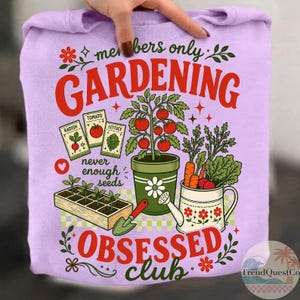Puede incluir: Una sudadera lila con un dise&ntilde;o de jardiner&iacute;a. El gr&aacute;fico incluye las palabras "members only GARDENING OBSESSED club" en rojo y verde, junto con ilustraciones de verduras, sobres de semillas y herramientas de jardiner&iacute;a.