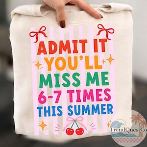 May include: Cream-colored sweatshirt with the text "ADMIT IT YOU'LL MISS ME 6-7 TIMES THIS SUMMER" in bright colors. The design includes pink stripes, bows, stars, and cherries. The sweatshirt is held up by a person.