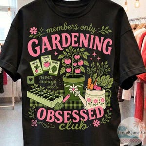 Puede incluir: Camiseta negra con un dise&ntilde;o de jardiner&iacute;a. El dise&ntilde;o incluye las palabras "members only GARDENING OBSESSED club" en rosa, junto con ilustraciones de plantas, semillas y herramientas de jardiner&iacute;a. La camiseta tiene cuello redondo y mangas cortas.