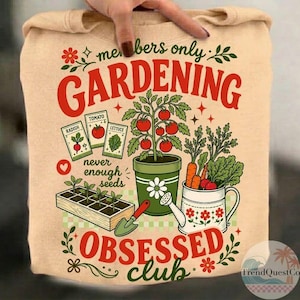 Puede incluir: Sudadera beige con tem&aacute;tica de jardiner&iacute;a. El dise&ntilde;o incluye las palabras "Gardening Obsessed Club" en rojo y verde, junto con ilustraciones de verduras, sobres de semillas y herramientas de jardiner&iacute;a. Tambi&eacute;n se incluye el texto "never enough seeds".
