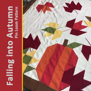 May include: A white knitted blanket with a fall theme. The blanket features a pumpkin, leaves, and a brown border. The text "Falling into Autumn Pin Loom Pattern" is in the upper left corner.