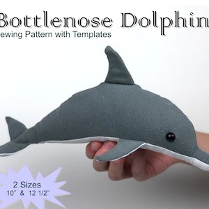Peut inclure: Un jouet en tissu rembourré en forme de dauphin gris et blanc avec des yeux noirs. Le jouet mesure 25,4 cm ou 31,75 cm de long. Le jouet est tenu par une main. Le texte "Bottlenose Dolphin Sewing Pattern with Templates" et "2 Sizes 10" & 12 1/2" est visible sur l'image.