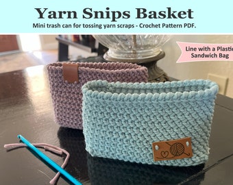 May include: Two crocheted yarn baskets, one in a light blue color and one in a mauve color. Both baskets have a brown leather label with a crochet hook and yarn ball design. The text "Line with a Plastic Sandwich Bag" is written in pink on a white background.