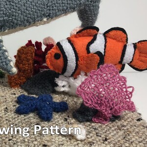 May include: A felt sewing pattern for a grey shark, orange and white clownfish, pink coral, blue starfish, and brown and grey rocks. The pattern includes the text "Sewing Pattern".