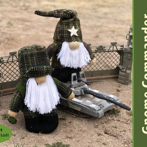May include: Two green and black camouflage gnome figures with white beards, one with a white star on its hat, standing in front of a toy tank. The gnome on the left is 11 inches tall. The text "Gnome Commander Pin Loom Pattern PDF" is in the upper right corner of the image.