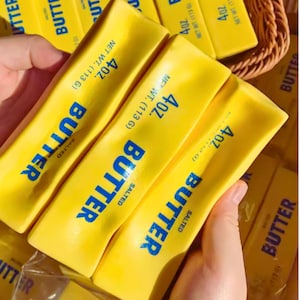 Op de afbeelding: Afbeelding van verschillende pakjes gezouten boter. Elk pakje zit in een gele verpakking met het woord "BUTTER" in grote blauwe letters. De verpakking geeft ook een nettogewicht van 113 g aan.