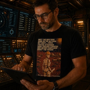 May include: Black t-shirt with the text "MEET THE NEW BOSS" and a robot illustration. The person in the image is wearing glasses and holding a tablet. The background shows control panels and screens.