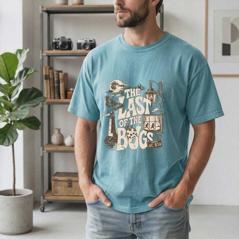 Puede incluir: Una camiseta de manga corta color verde azulado con un estampado gr&aacute;fico que incluye el texto "THE LAST OF THE BUGS". El dise&ntilde;o presenta ilustraciones de un faro, una mariquita, un farol, una luna y una ventana con dos siluetas.