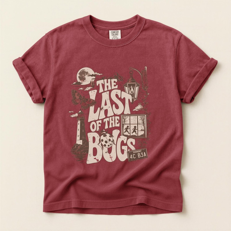 Puede incluir: Una camiseta de manga corta de color rojo oscuro con un estampado gr&aacute;fico en crema y marr&oacute;n. El dise&ntilde;o incluye una luna, un faro, un farol, una mariquita y una ventana con dos figuras, junto con el texto THE LAST OF THE BUGS y una matr&iacute;cula de Vermont.