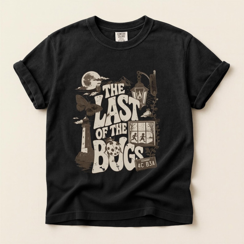 Puede incluir: Una camiseta negra de manga corta con un estampado gr&aacute;fico que incluye el texto THE LAST OF THE BUGS. El dise&ntilde;o muestra un faro, una polilla, una luna, un farol, una ventana con dos siluetas y una matr&iacute;cula de Vermont con el texto 4C B3A.