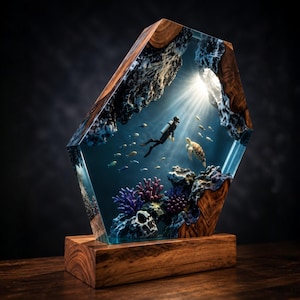 Könnte beinhalten: Eine sechseckige Skulptur aus Harz und Holz mit einer Unterwasserszene, die einen Taucher, eine Meeresschildkröte und kleine Fische zeigt, die zwischen violetten und dunklen Korallenformationen schwimmen. Lichtstrahlen fallen von oben ein.