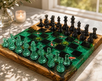 Op de afbeelding: Een schaakspel met een bord van natuurlijk hout en doorschijnende groene hars met ingebedde koikarpers en mosaccenten. De set bevat een set doorschijnende groene glazen schaakstukken en een set donkere metalen schaakstukken.