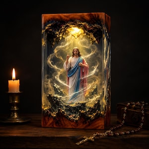 May include: A rectangular resin lamp featuring a central figurine of a bearded man in white, blue, and pink robes with one hand raised. The figure stands amidst dark, jagged rock formations surrounded by swirling golden light and smoke effects.