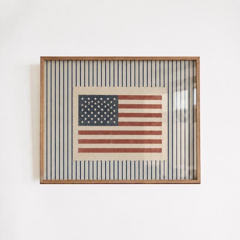 Puede incluir: Una impresi&oacute;n rectangular enmarcada que presenta una ilustraci&oacute;n centrada de la bandera de los Estados Unidos con una textura desgastada. La bandera se sit&uacute;a sobre un fondo de rayas verticales azul marino sobre un campo de color crema.