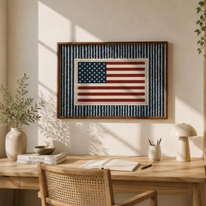 May include: Framed artwork featuring the American flag. The flag design includes red and white stripes and a field of white stars on a blue background. The artwork is set against a blue and white striped background and framed in a dark wood.