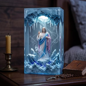 Può includere: Una lampada rettangolare in resina con una statuetta centrale di Gesù Cristo in piedi all'interno di una caverna ghiacciata con stalattiti pendenti e formazioni rocciose bluastre. La scena è illuminata dall'alto, creando un effetto luminoso con volute di fumo bianco.