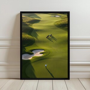 Può includere: Una stampa artistica da parete incorniciata che mostra una vista aerea di un campo da golf con fairway verdi ondulati, bunker di sabbia e diverse piccole figure di persone che camminano sull'erba sotto una luce soffusa, in cornice nera.