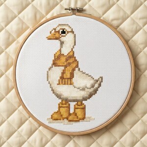 Op de afbeelding: Een kruissteekring met een witte gans met een sjaal en laarzen. De gans heeft een gele snavel en staat tegen een witte achtergrond. De houten ring heeft een diameter van ongeveer 20 cm en de achtergrond is een gewatteerde stof.