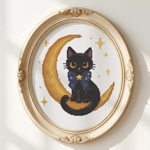 May include: A cross-stitch embroidery featuring a black cat with large yellow eyes and a blue bow with a gold star, sitting on a golden crescent moon. The design is surrounded by small gold stars and is displayed in an ornate oval cream frame.