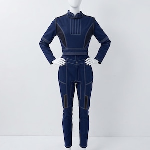Op de afbeelding: Een donkerblauwe tweedelige outfit bestaande uit een top met lange mouwen en een opstaande kraag, gecombineerd met een bijpassende broek. De set is voorzien van opvallende witte stiksels en zwarte accentpanelen op de schouders en benen.