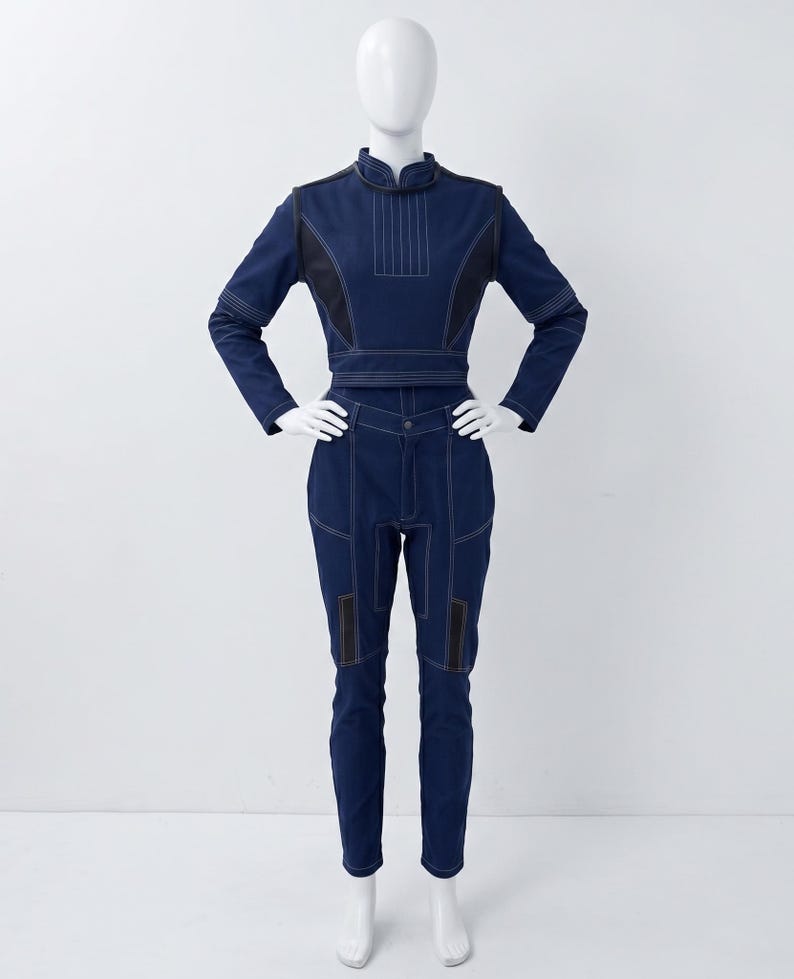 Op de afbeelding: Een donkerblauwe tweedelige outfit bestaande uit een top met lange mouwen en een opstaande kraag, gecombineerd met een bijpassende broek. De set is voorzien van opvallende witte stiksels en zwarte accentpanelen op de schouders en benen.